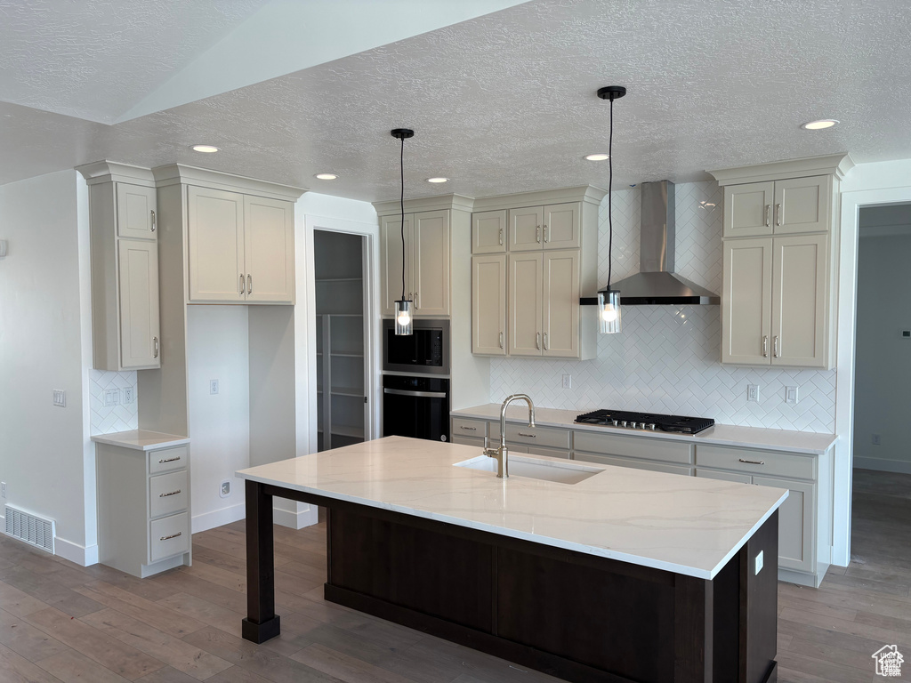 Kitchen with a sink, decorative backsplash, wall chimney exhaust hood, appliances with stainless steel finishes, and visible vents