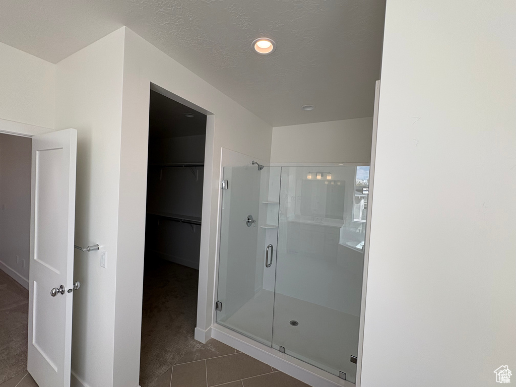 Full bath featuring tile patterned floors, baseboards, a shower stall, and a walk in closet