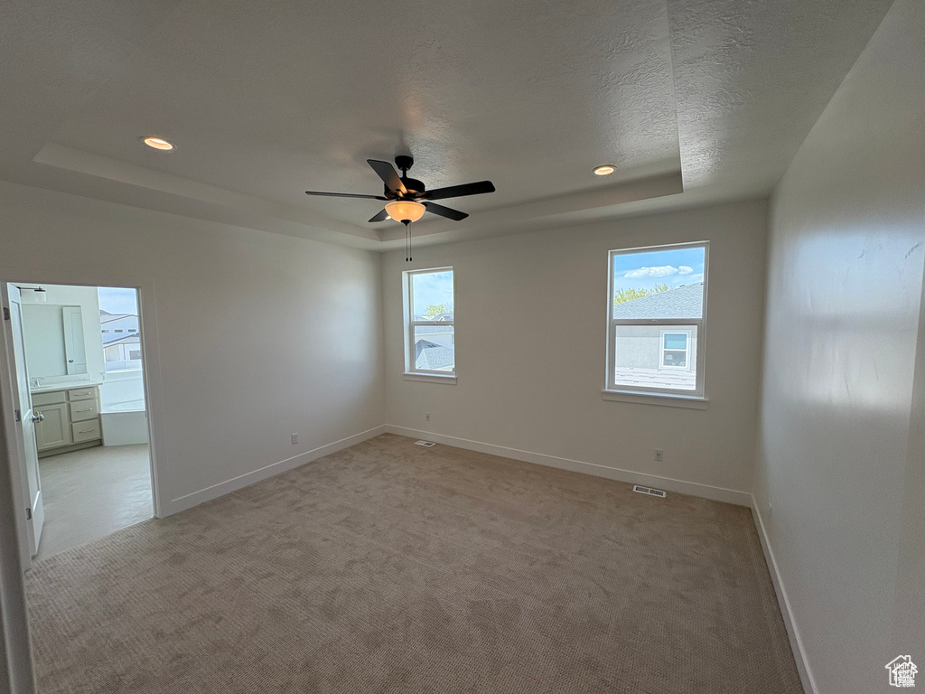 Unfurnished room featuring a raised ceiling, visible vents, baseboards, light colored carpet, and ceiling fan