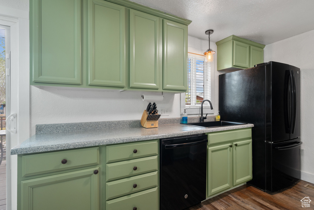 Kitchen featuring green cabinetry, light countertops, a sink, dark wood-type flooring, and black appliances