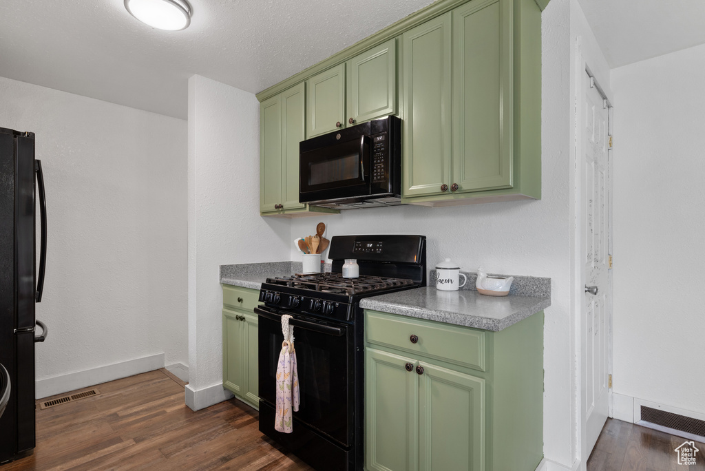 Kitchen with visible vents, baseboards, green cabinets, dark wood-type flooring, and black appliances