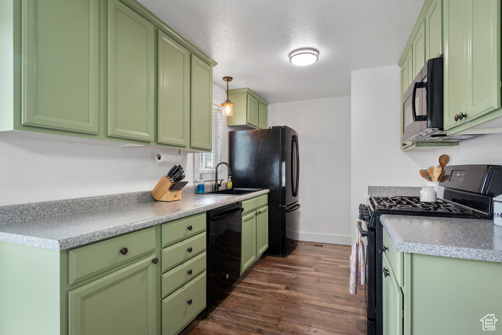Kitchen featuring a sink, black appliances, dark wood finished floors, baseboards, and green cabinetry