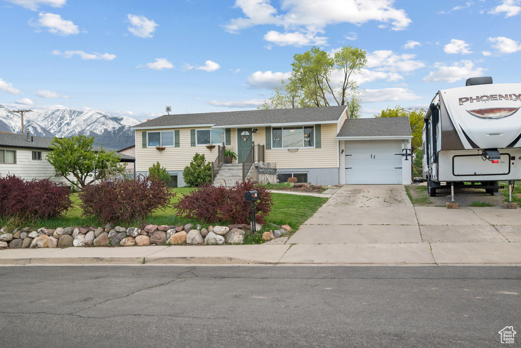 View of front of property with a mountain view, driveway, a shingled roof, and a garage