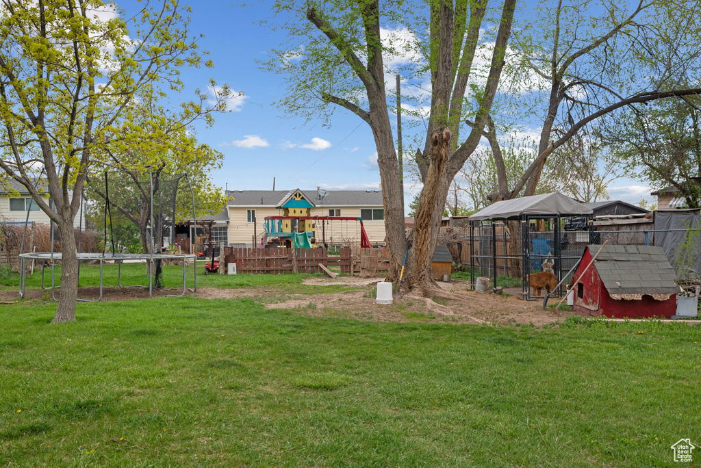 View of yard featuring an outbuilding, exterior structure, a playground, fence, and a trampoline