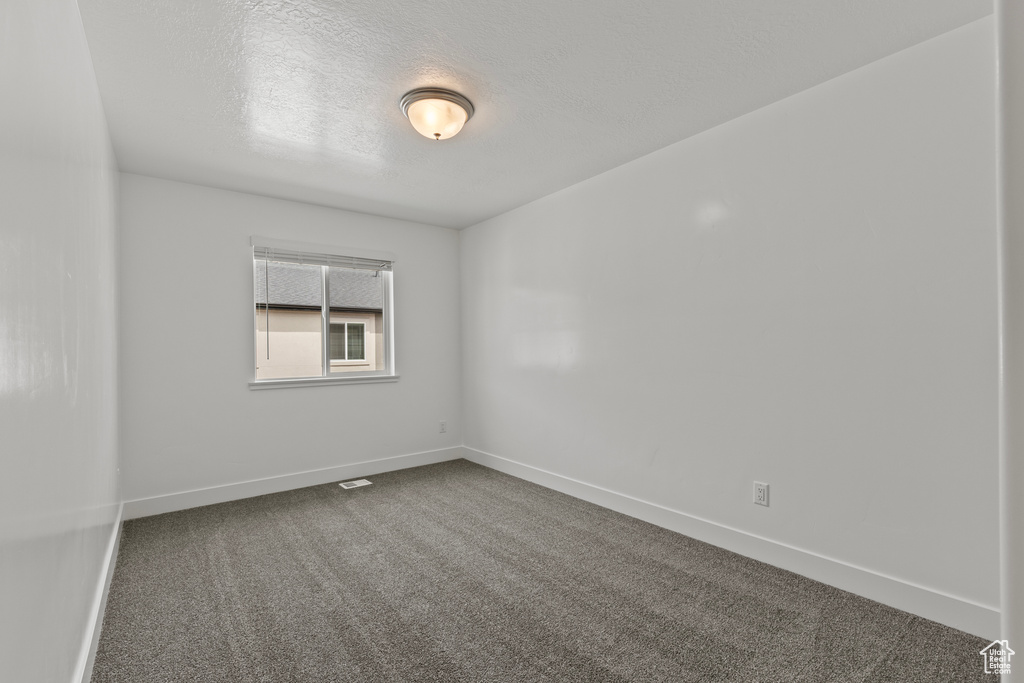 Empty room featuring dark colored carpet, a textured ceiling, and baseboards