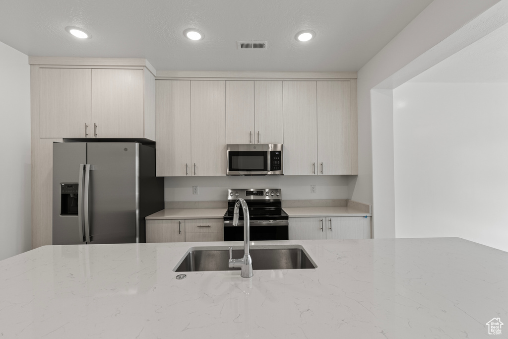 Kitchen with light stone countertops, stainless steel appliances, a sink, and recessed lighting