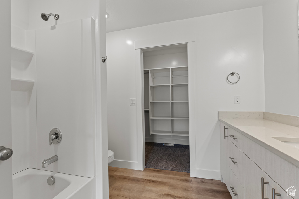 Bathroom with wood finished floors, shower / bathtub combination, toilet, vanity, and baseboards