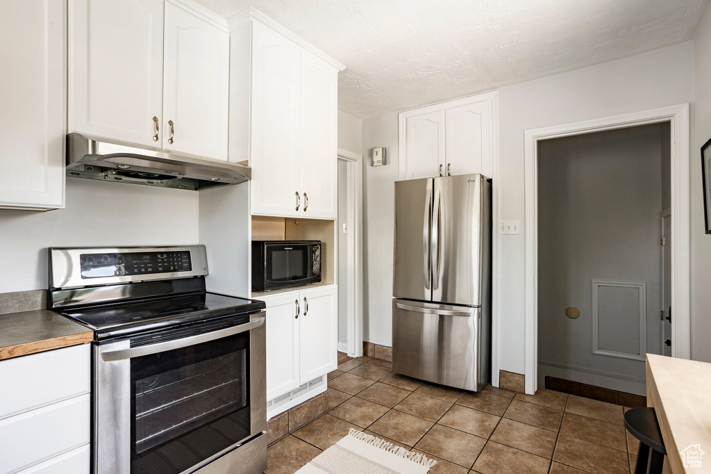 Kitchen with stainless steel appliances, under cabinet range hood, white cabinetry, and tile patterned flooring