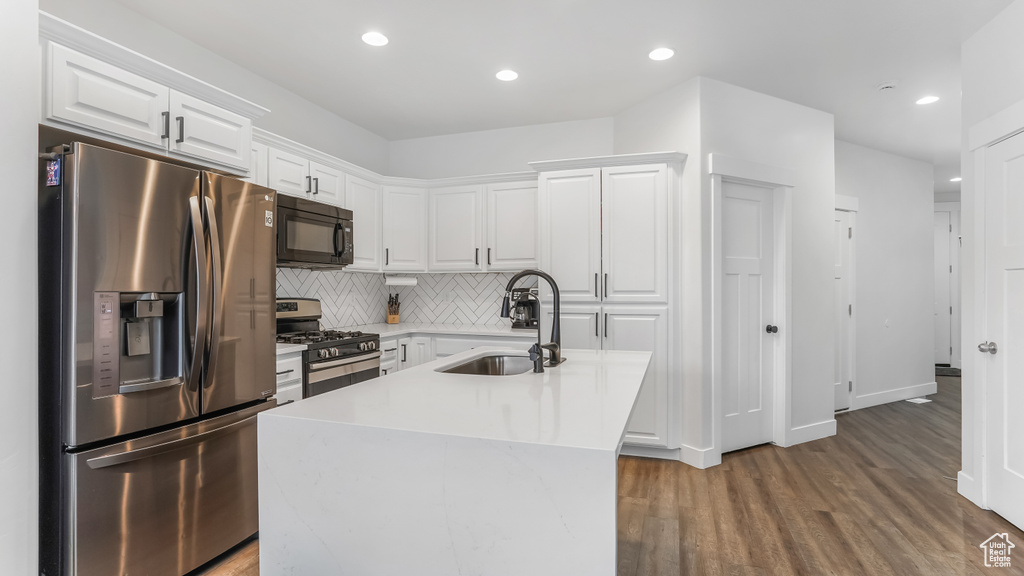 Kitchen with white cabinets, stainless steel appliances, wood finished floors, a sink, and decorative backsplash