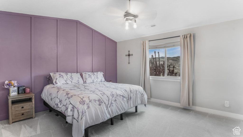 Bedroom with vaulted ceiling, a decorative wall, ceiling fan, light colored carpet, and visible vents