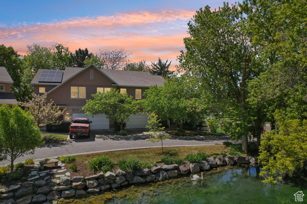 View of front of house with concrete driveway, a garage, a shingled roof, and solar panels
