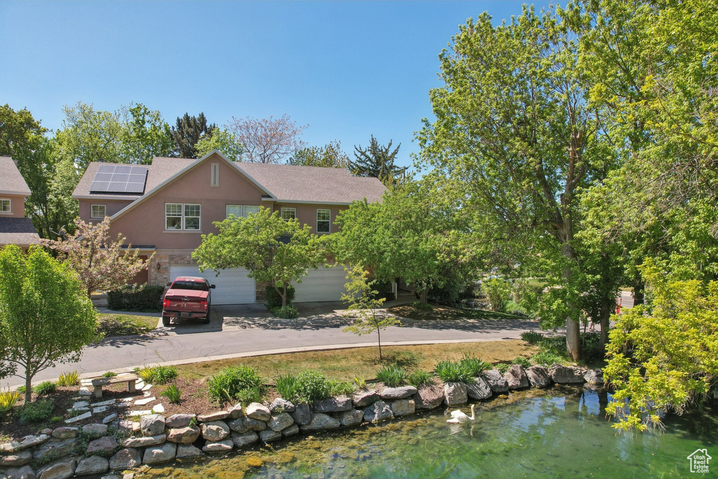 View of front of home with stone siding, stucco siding, an attached garage, driveway, and solar panels