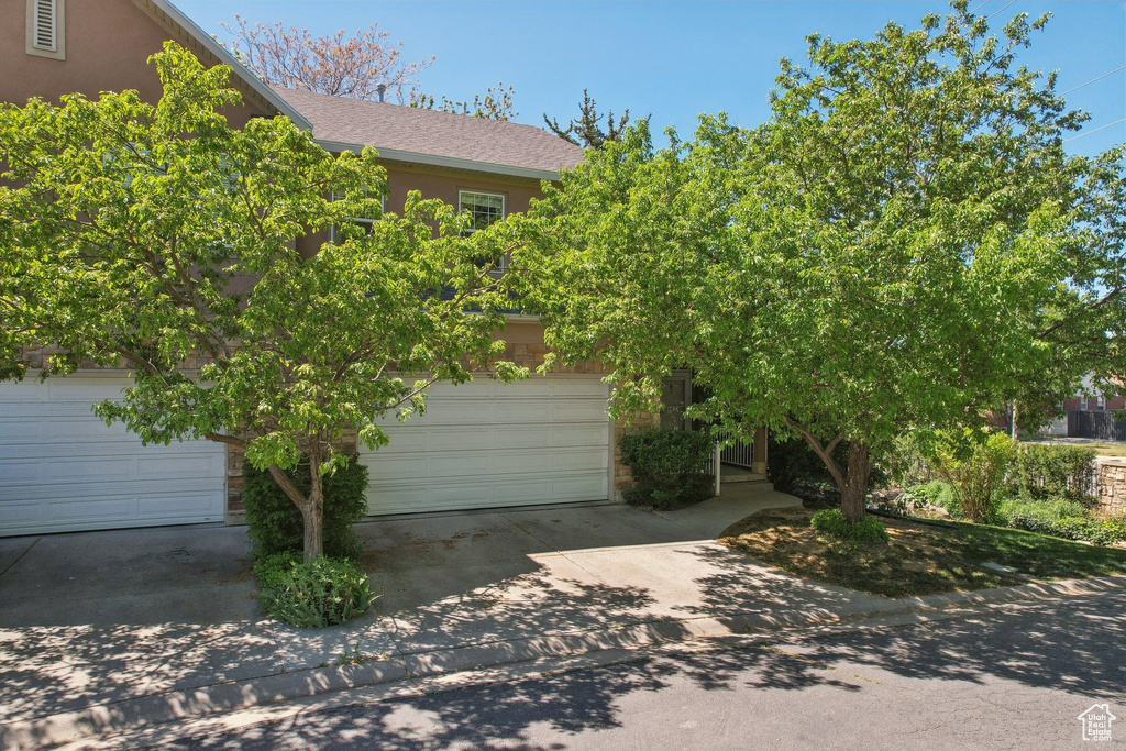 View of front of house with an attached garage, driveway, roof with shingles, and stucco siding