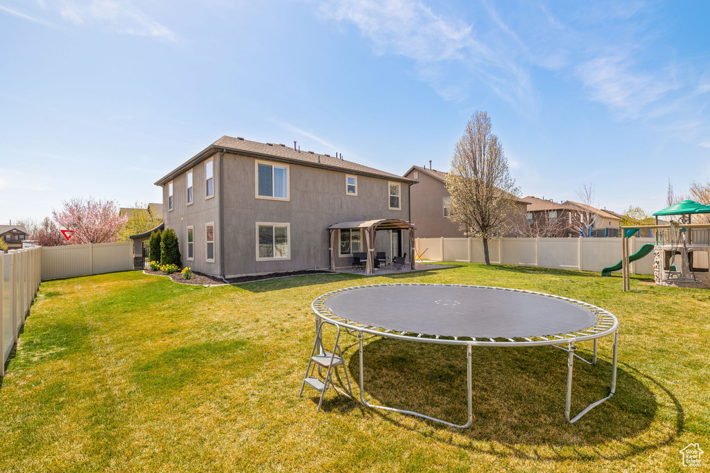 Back of property with a fenced backyard, a playground, a trampoline, and a lawn