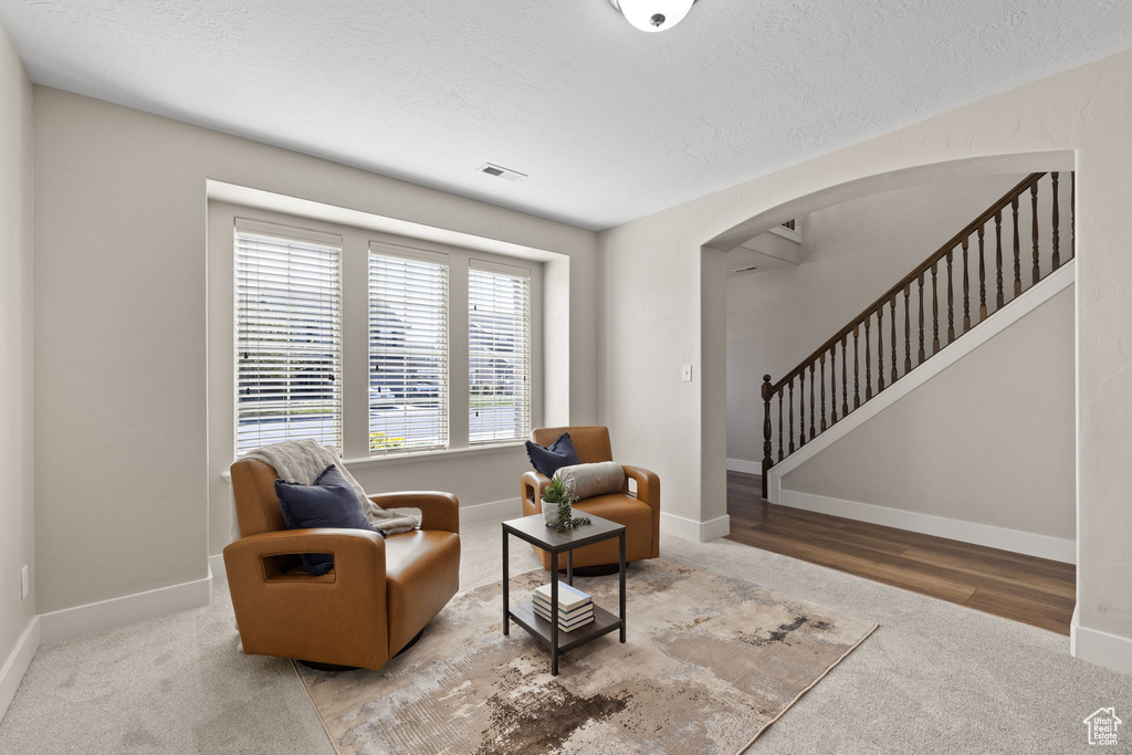 Sitting room featuring stairs, arched walkways, carpet floors, baseboards, and visible vents