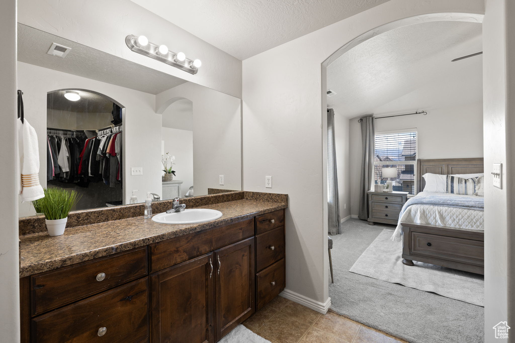 Ensuite bathroom featuring a textured ceiling, visible vents, tile patterned flooring, vanity, and connected bathroom