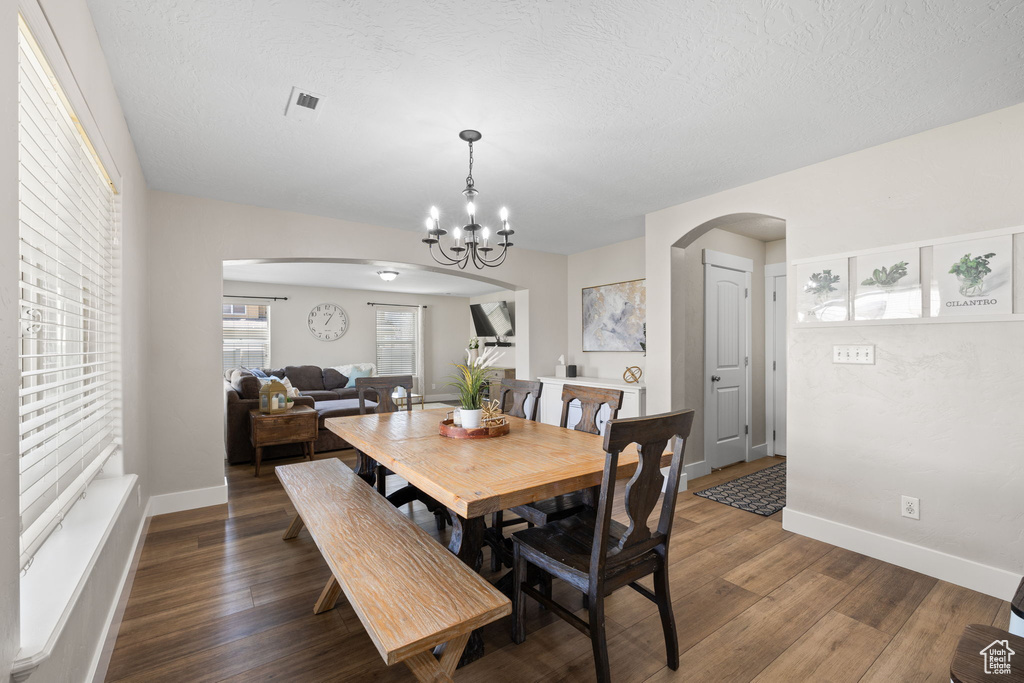 Dining area featuring arched walkways, a chandelier, wood finished floors, and visible vents