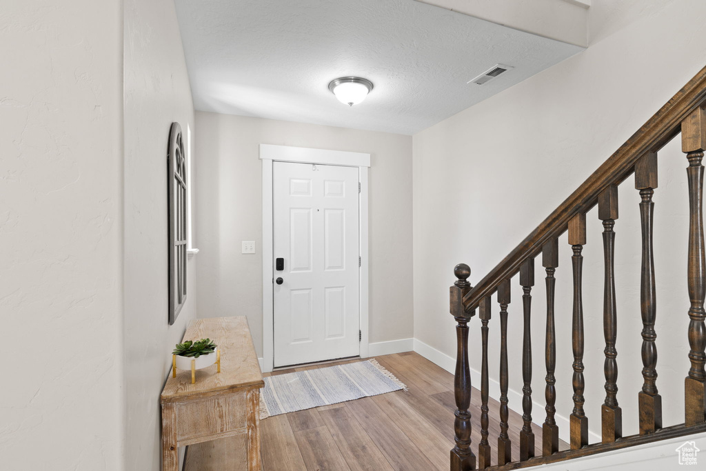 Entrance foyer featuring a textured ceiling, visible vents, baseboards, wood finished floors, and stairway