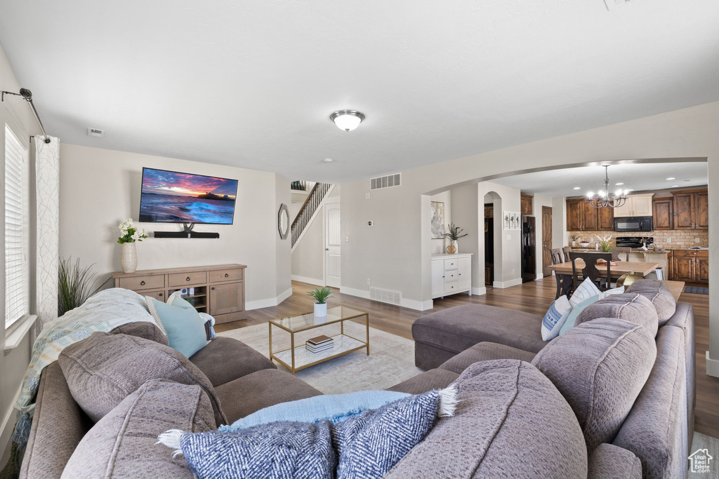 Living room with light wood finished floors, an inviting chandelier, visible vents, and arched walkways