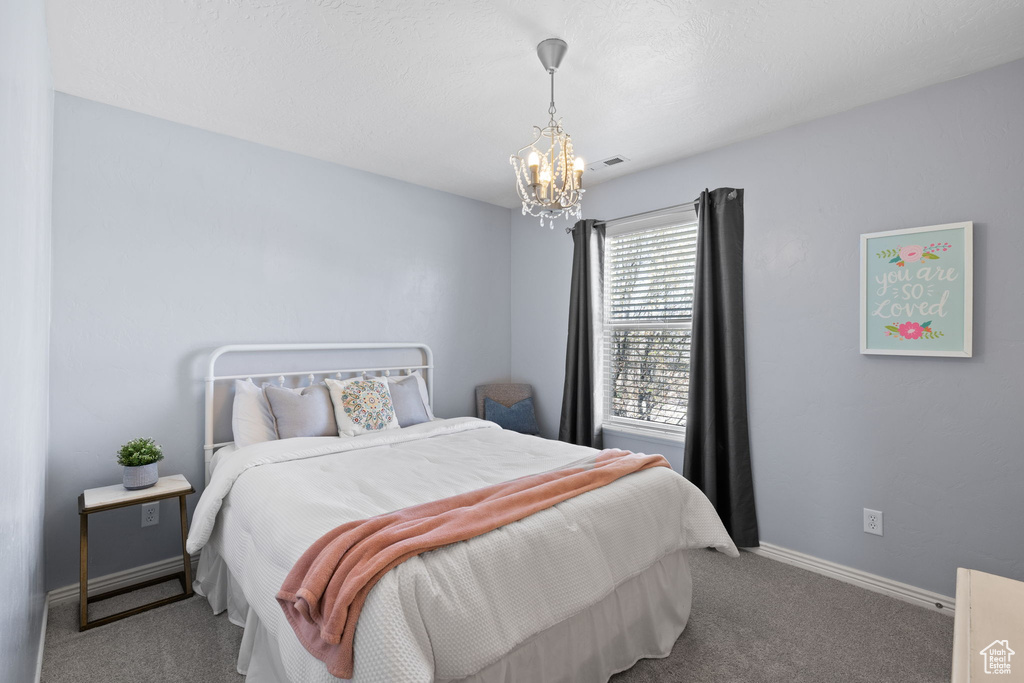 Carpeted bedroom featuring visible vents, baseboards, and a notable chandelier