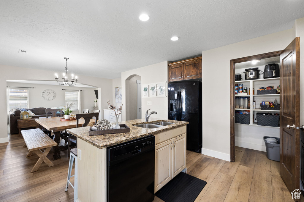 Kitchen featuring a kitchen island with sink, light wood-style flooring, arched walkways, a sink, and black appliances