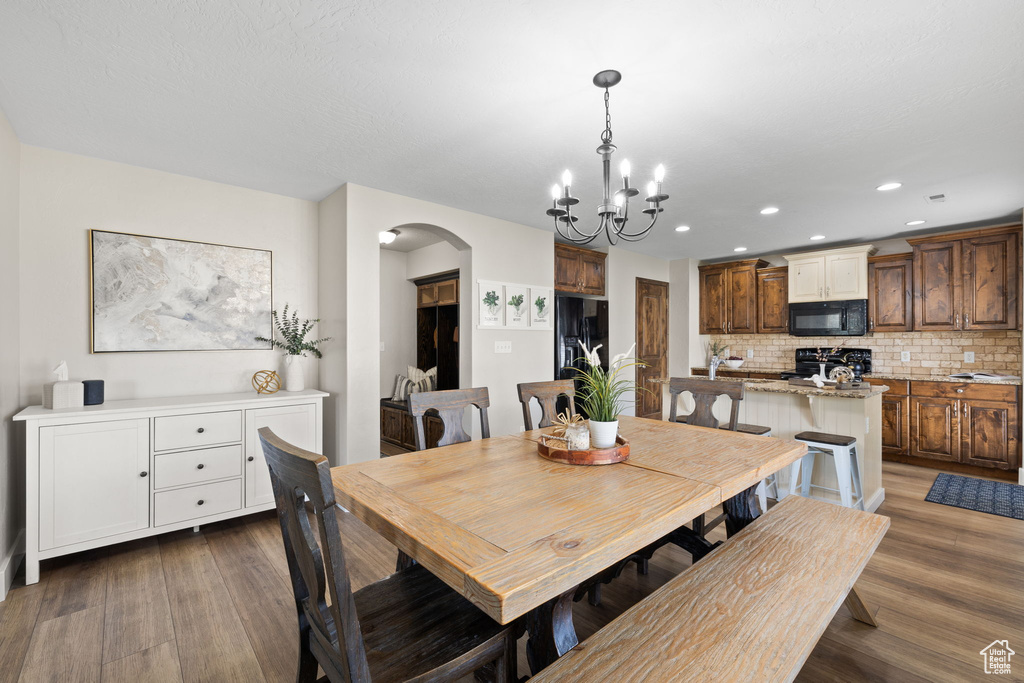 Dining room featuring arched walkways, a chandelier, wood finished floors, and recessed lighting