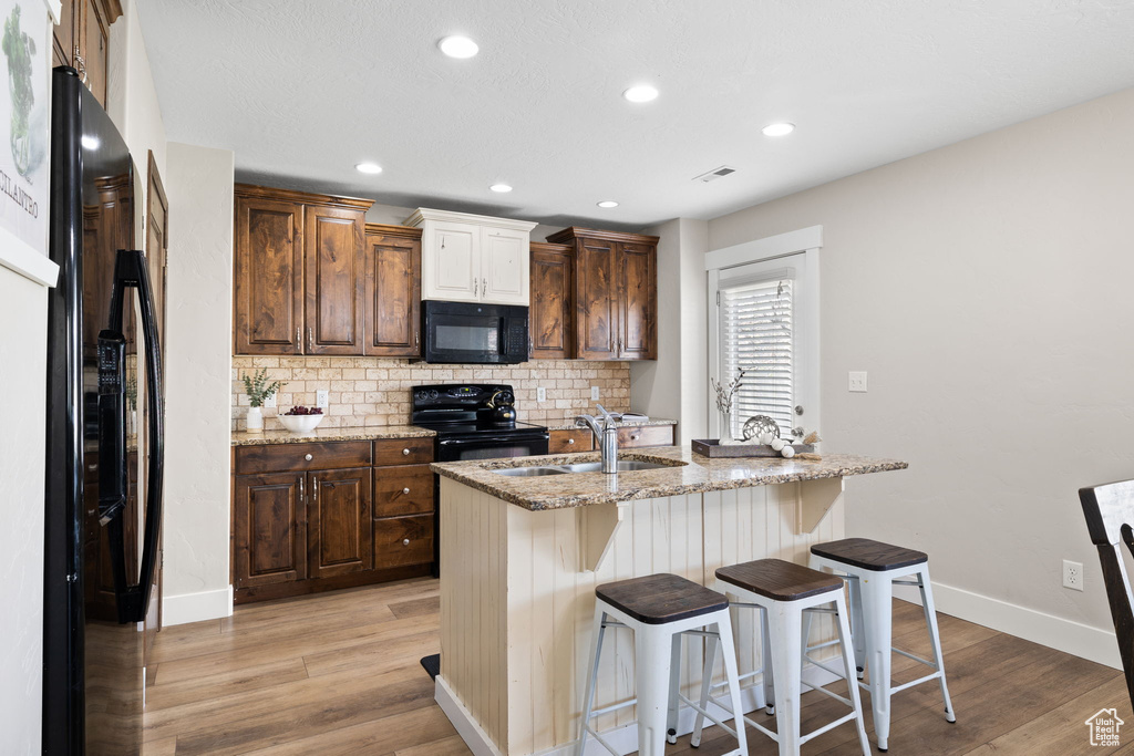 Kitchen featuring light wood finished floors, a kitchen breakfast bar, a sink, backsplash, and black appliances
