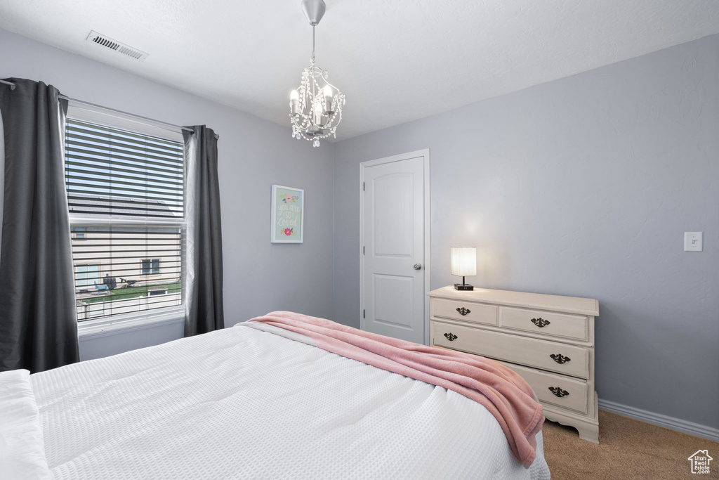 Bedroom with light colored carpet, an inviting chandelier, visible vents, and baseboards