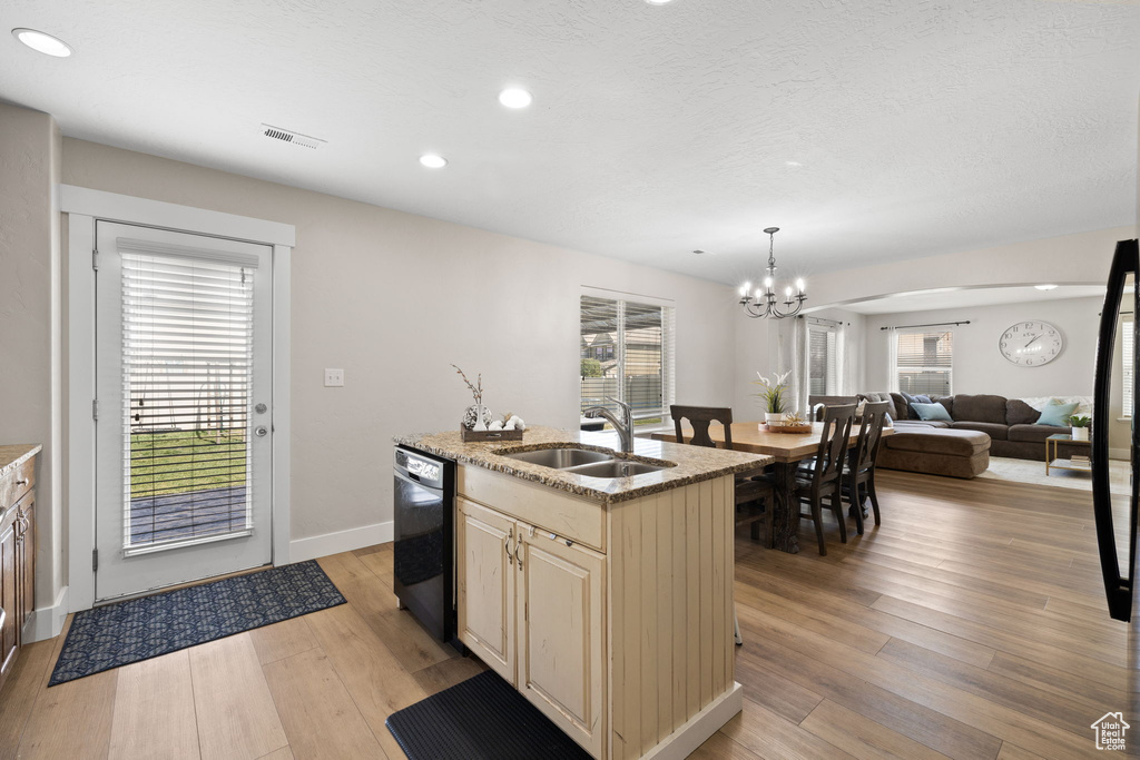 Kitchen with a sink, a chandelier, cream cabinets, light stone countertops, and visible vents