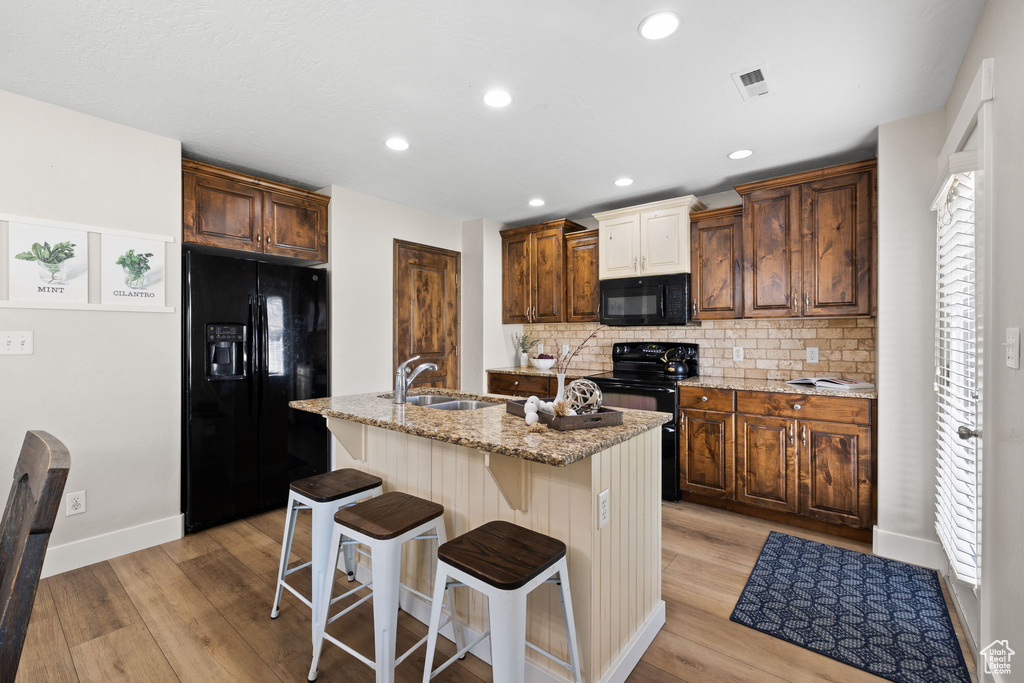 Kitchen with light wood finished floors, a sink, black appliances, and tasteful backsplash