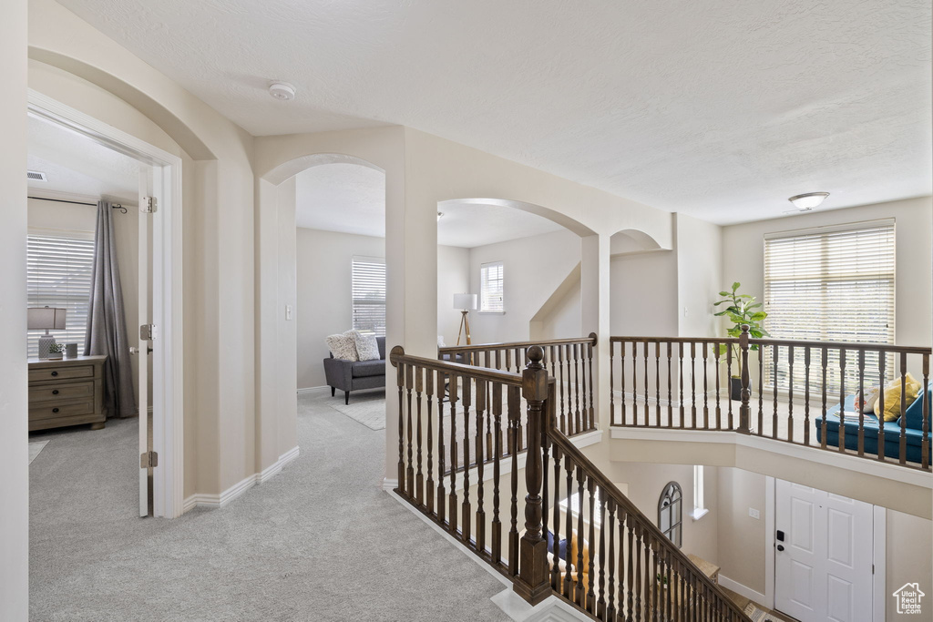 Corridor with arched walkways, baseboards, carpet floors, and an upstairs landing