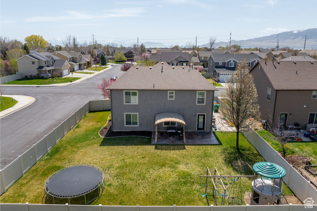 Rear view of house with a fenced backyard, a mountain view, a residential view, and a lawn