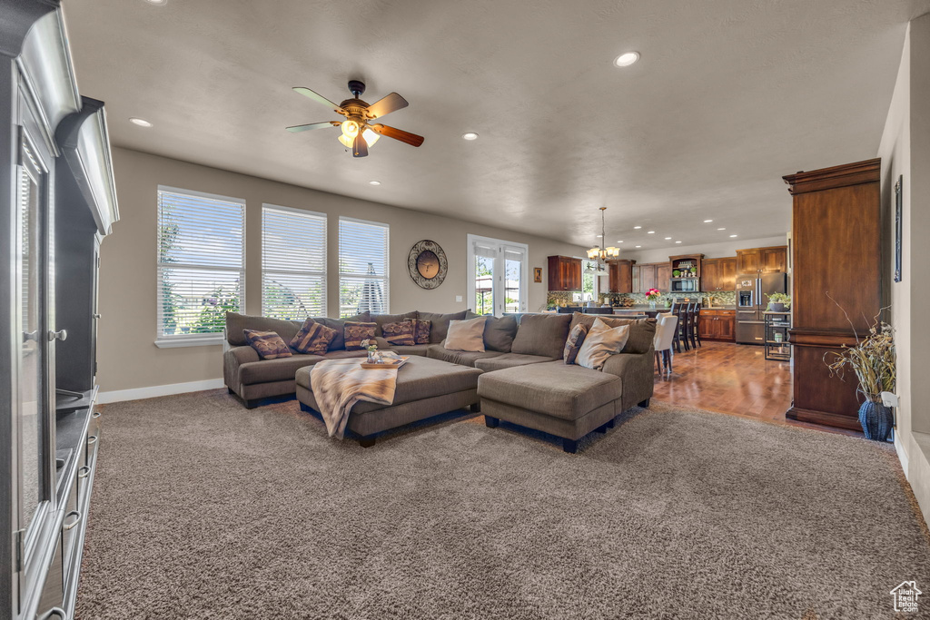 Carpeted living area with healthy amount of natural light, recessed lighting, a chandelier, ceiling fan, and baseboards
