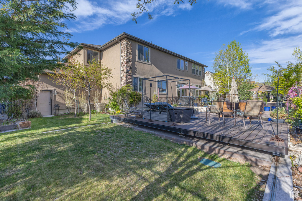 Back of house featuring stucco siding, a wooden deck, stone siding, and a yard