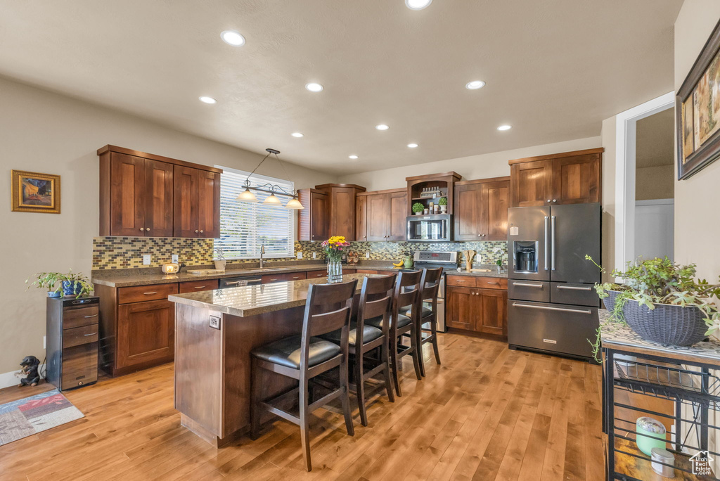 Kitchen with stainless steel appliances, a center island, a kitchen bar, light wood-style floors, and tasteful backsplash