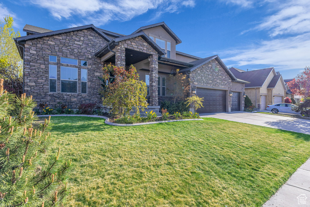 View of front of house featuring stone siding, concrete driveway, a front yard, and a garage