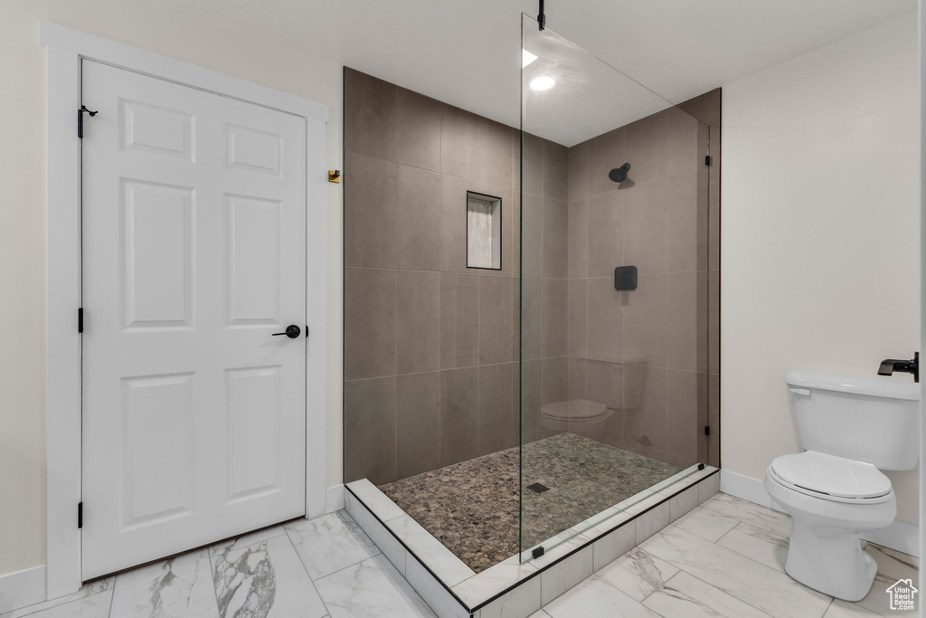 Bathroom with toilet, marble look tiles, tiled shower, and baseboards