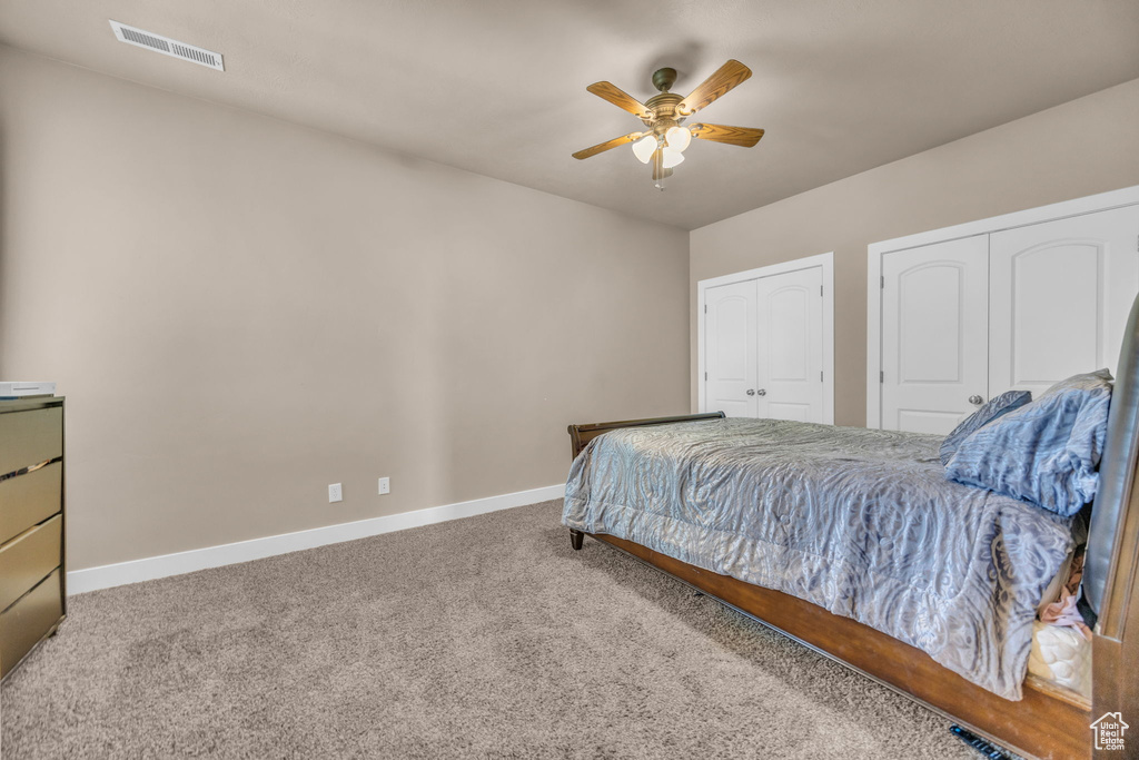 Carpeted bedroom with multiple closets, baseboards, and ceiling fan