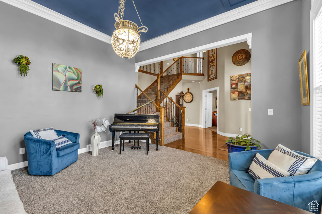 Living area with stairs, a chandelier, baseboards, carpet floors, and crown molding