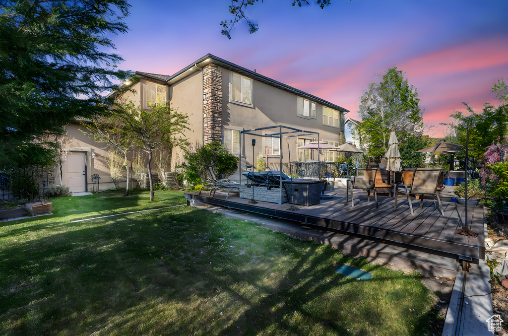 Back of property at dusk featuring stucco siding, a wooden deck, a yard, and stone siding