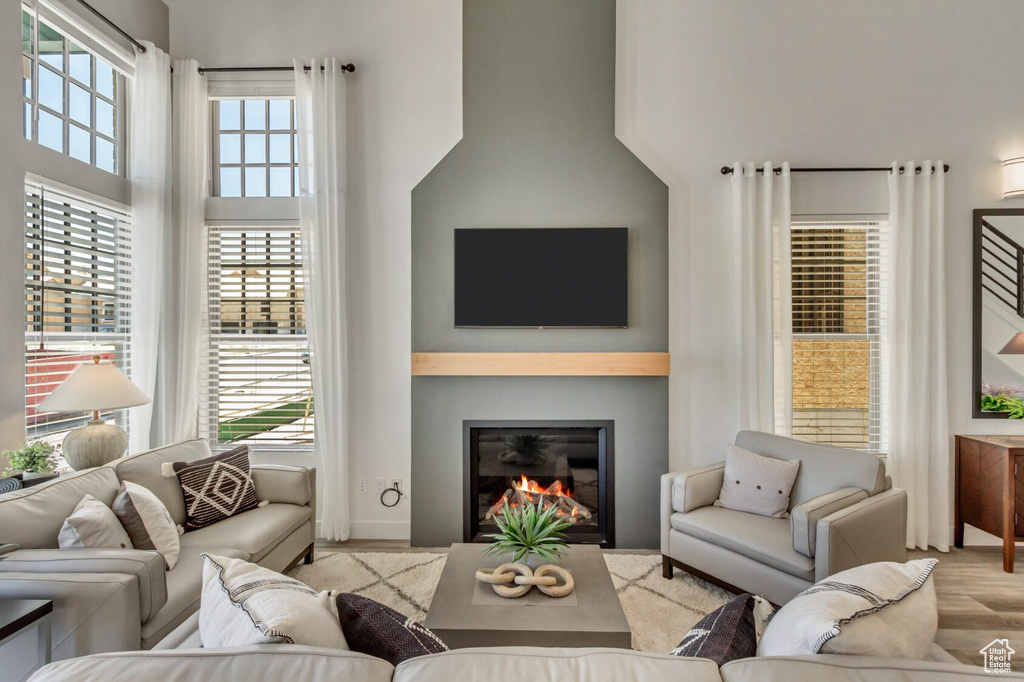 Living area featuring a glass covered fireplace, baseboards, wood finished floors, and a high ceiling