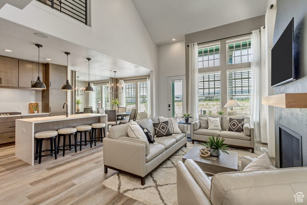Living area with recessed lighting, an inviting chandelier, a premium fireplace, light wood-type flooring, and high vaulted ceiling