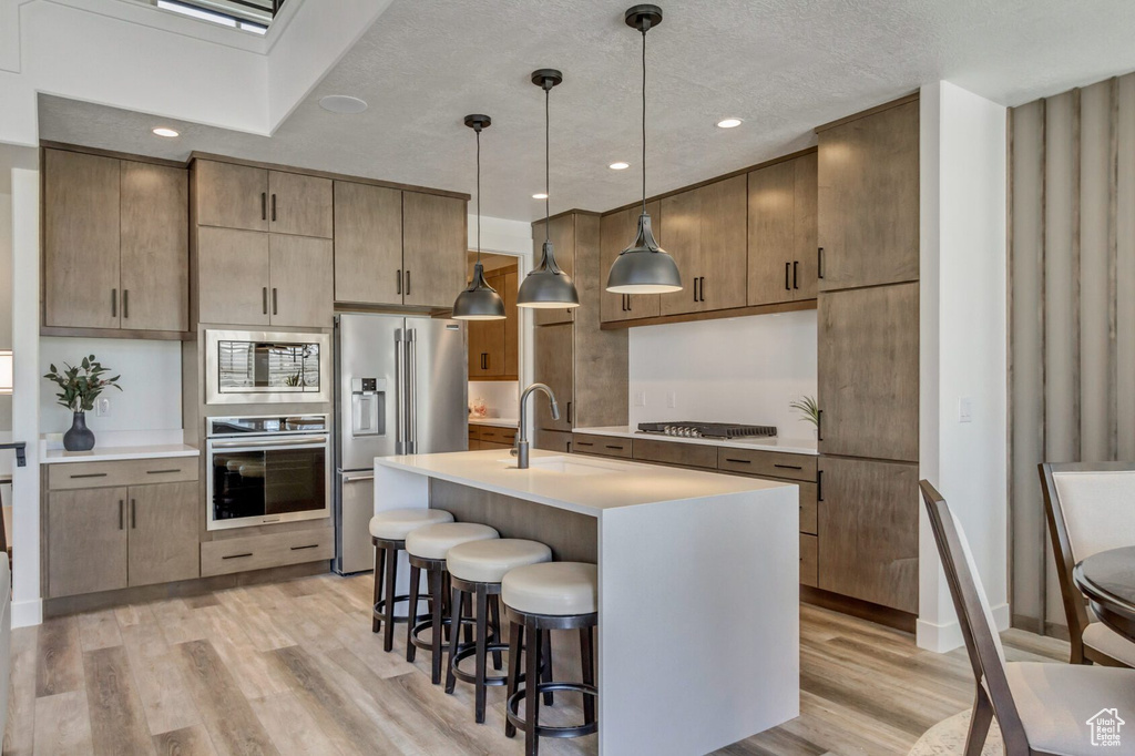 Kitchen featuring light wood-type flooring, a kitchen breakfast bar, stainless steel appliances, and a sink
