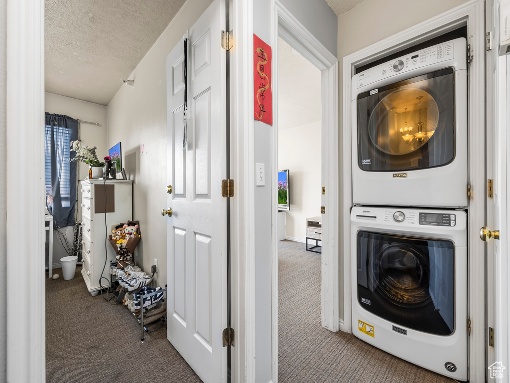 Clothes washing area featuring carpet, stacked washer and dryer, and a textured ceiling