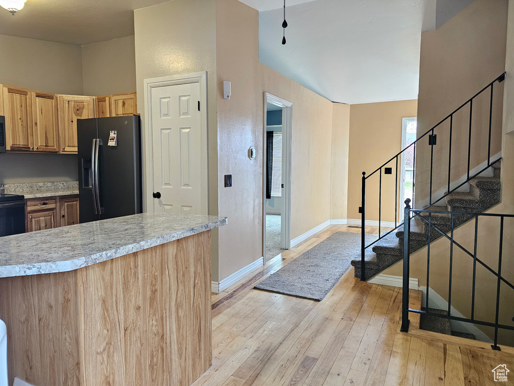 Kitchen featuring black fridge with ice dispenser, light countertops, light wood-type flooring, baseboards, and light brown cabinets