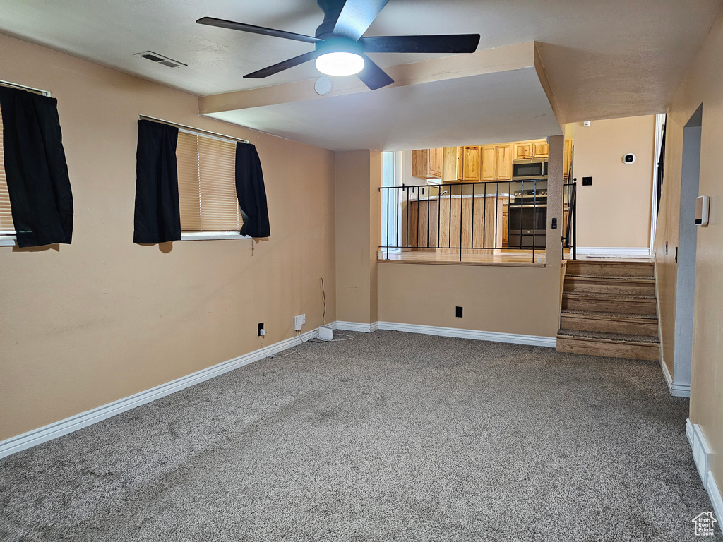 Carpeted empty room featuring ceiling fan, baseboards, and stairs