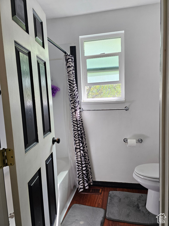 Bathroom featuring baseboards, wood finished floors, shower / tub combo with curtain, and toilet