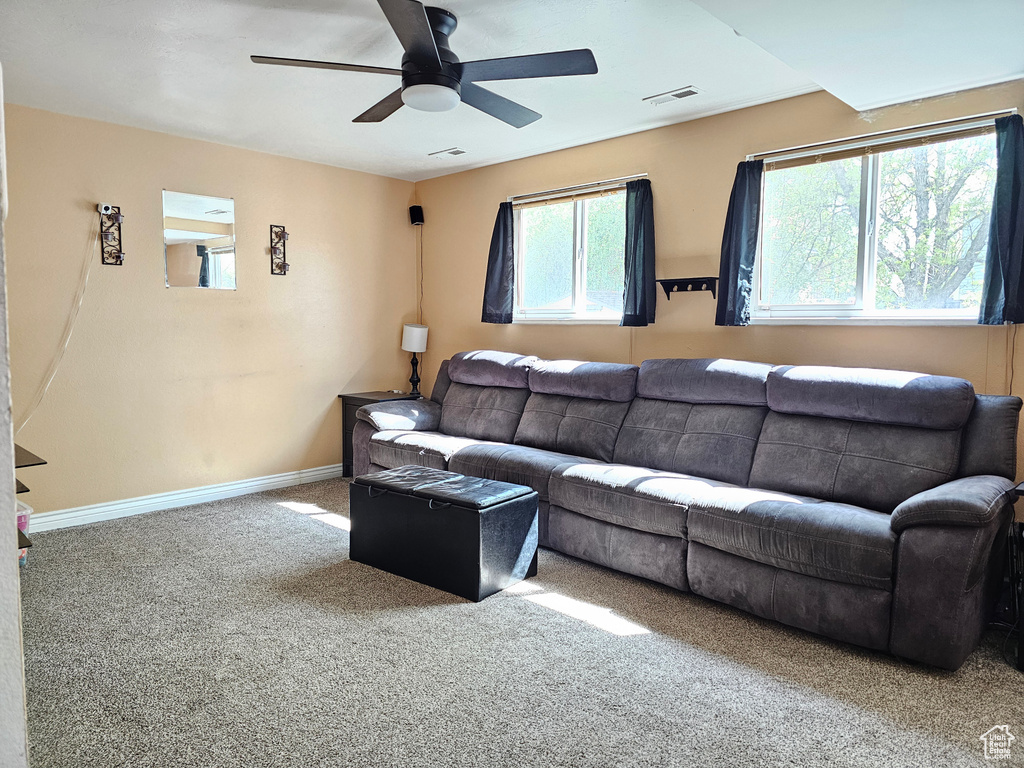 Carpeted living room with ceiling fan, baseboards, and visible vents