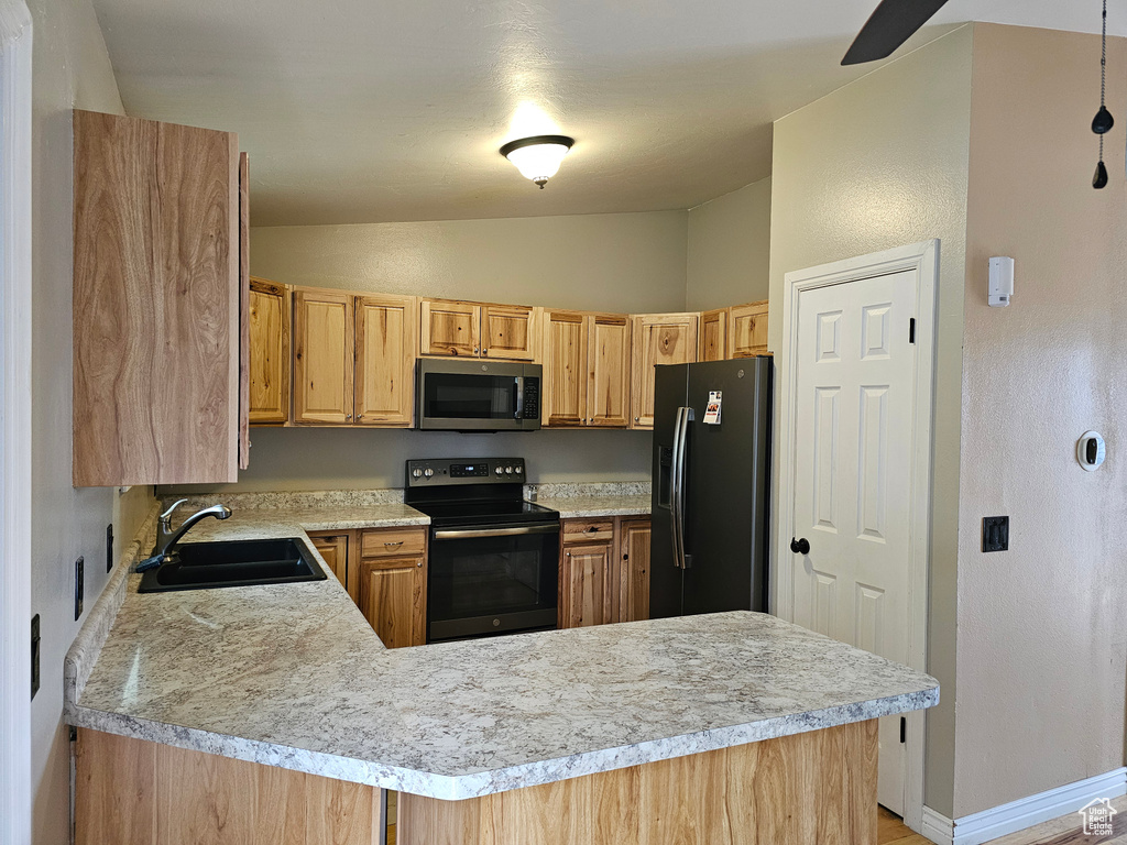 Kitchen featuring black appliances, a sink, vaulted ceiling, light countertops, and a peninsula