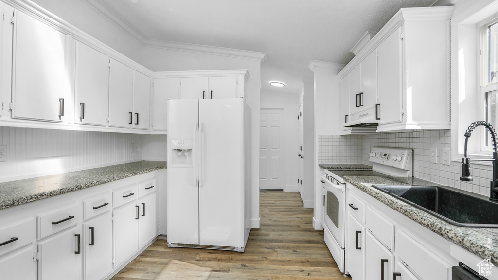Kitchen featuring under cabinet range hood, a sink, white appliances, tasteful backsplash, and light wood-style flooring